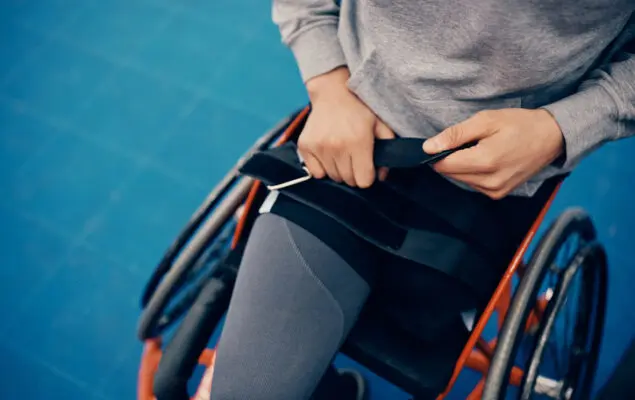 Unrecognizable athlete fastening belt on wheelchair while preparing to exercise on an outdoor court.